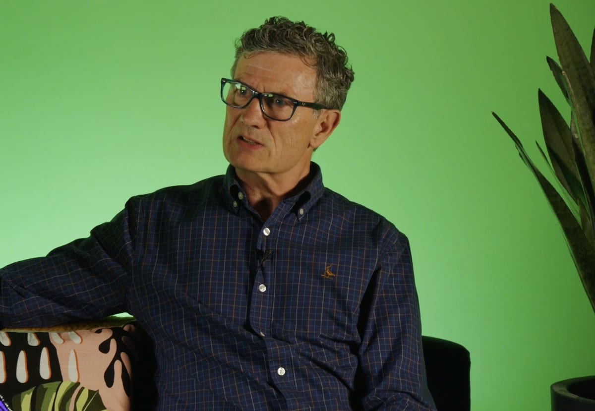 Alan Heap of Purple Monster talking on a sofa in front of a green backdrop