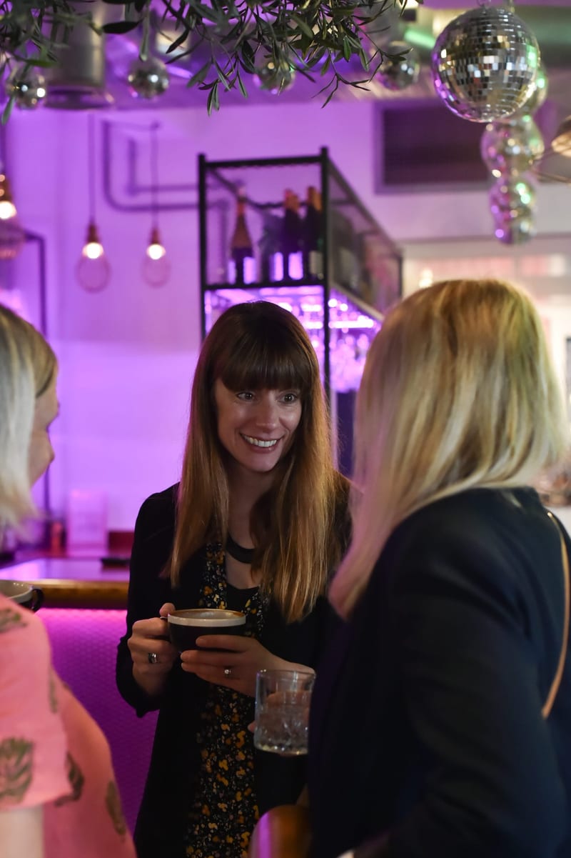 Two women chatting over coffee under pink lights at 1 Mill Street