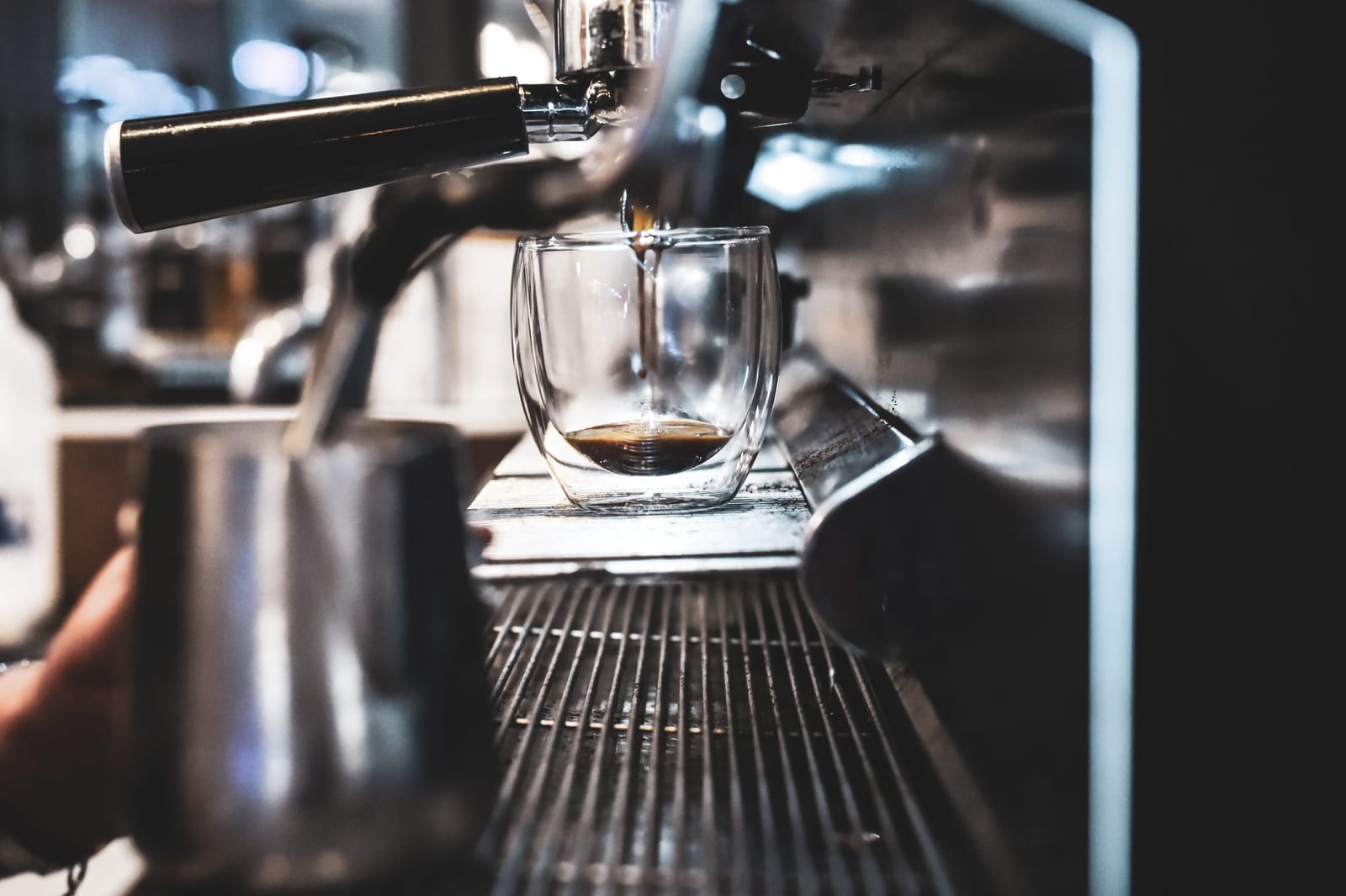 An espresso shot pouring from a coffee machine into a glass cup