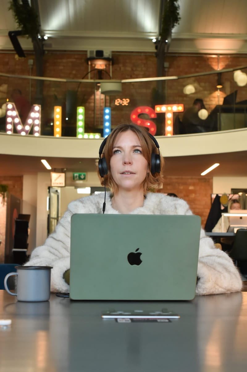 A member in headphones working on a laptop under the Mill St light-up letters