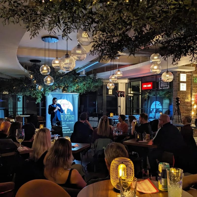 A speaker presenting to a seated evening audience under the tree at 1 Mill Street