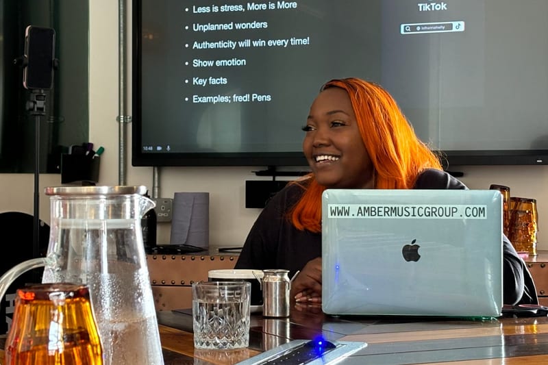 A speaker smiling at her laptop during a storytelling workshop at 1 Mill Street