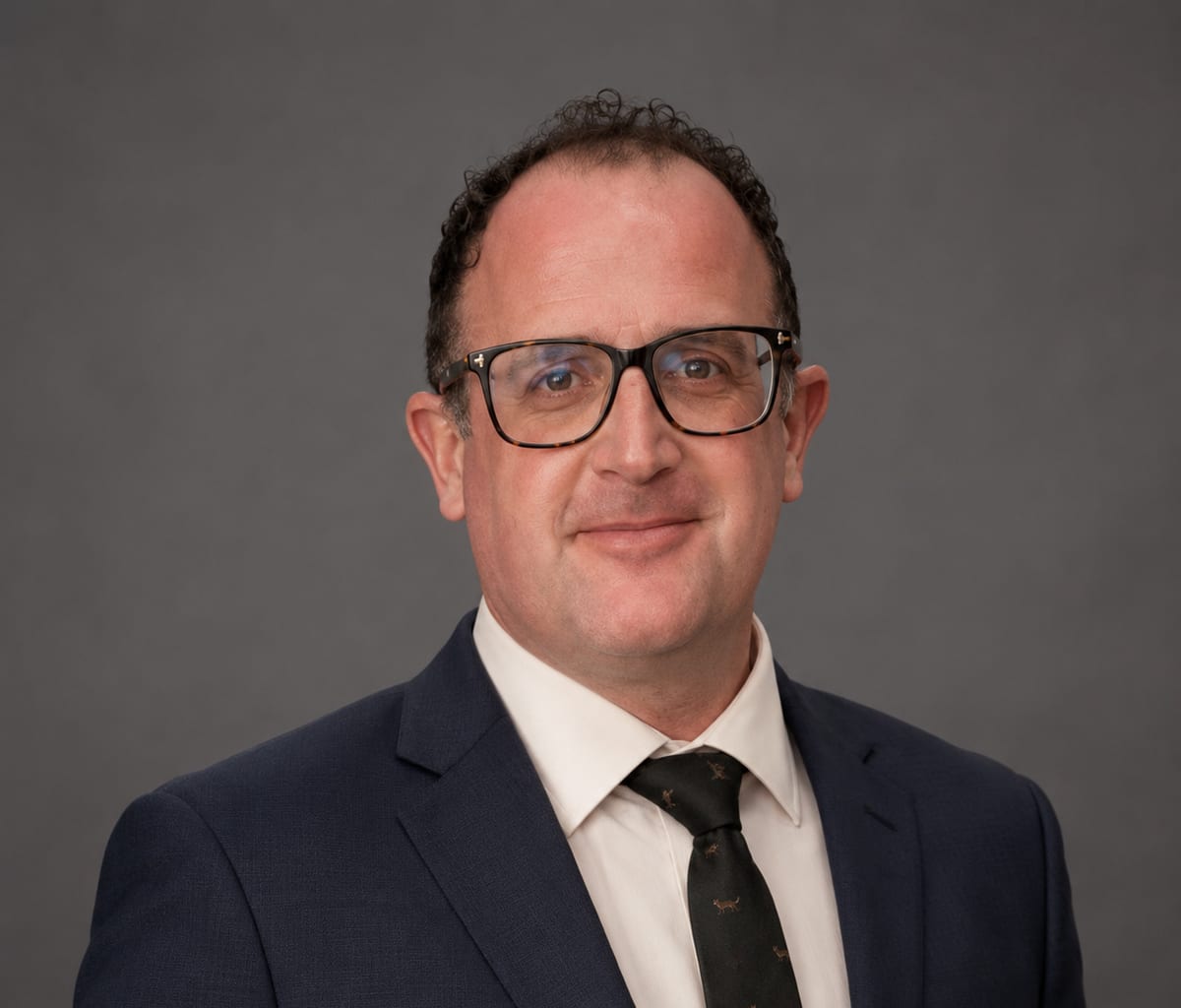 Headshot of Simon Prescott of Tutum Consulting in a navy suit and glasses